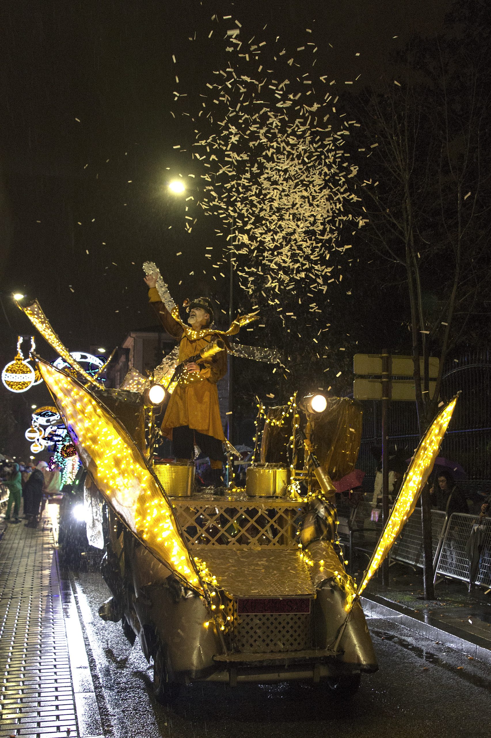 Un artista celebra desde una carroza dorada con alas de luz, lanzando una lluvia de confeti al cielo nocturno