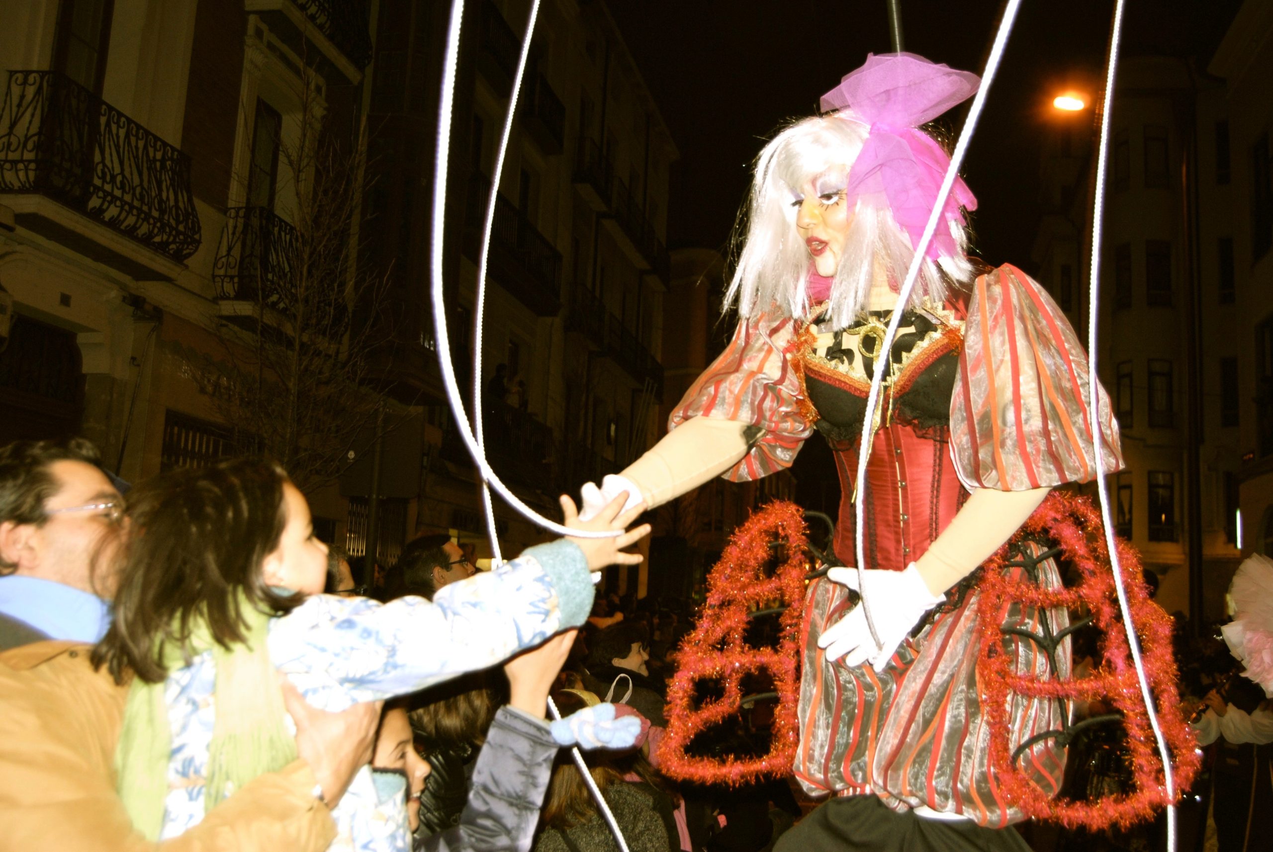 Una artista disfrazada de marioneta con peluca blanca y vestido rojo