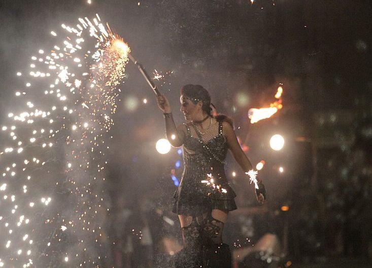 Una artista en zancos con un corsé de cuero blande una antorcha pirotécnica