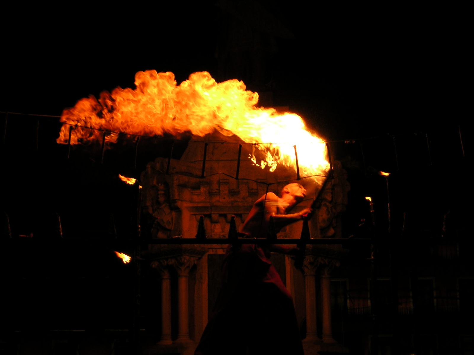 En la oscuridad de la noche, una intensa llamarada naranja y amarilla ilumina el centro de la escena.