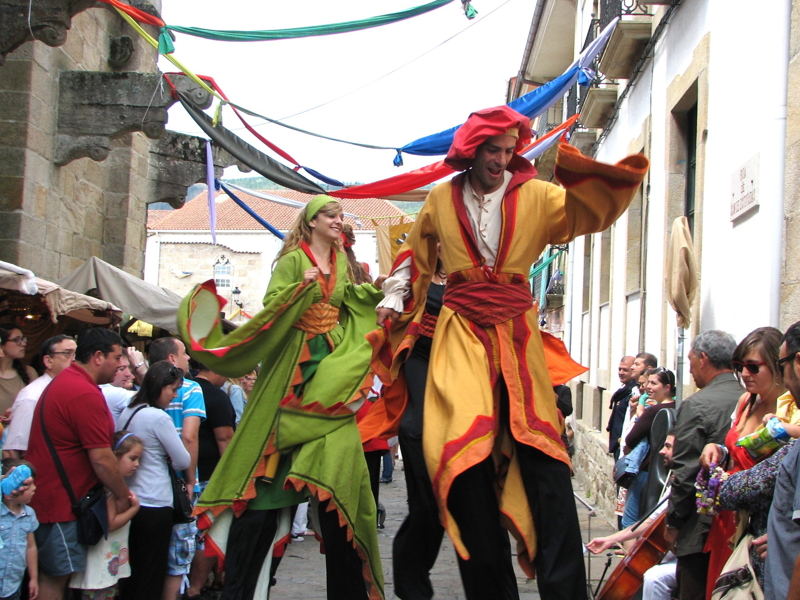 Dos zancudos con trajes medievales coloridos, ella de verde con detalles naranjas, y él de amarillo