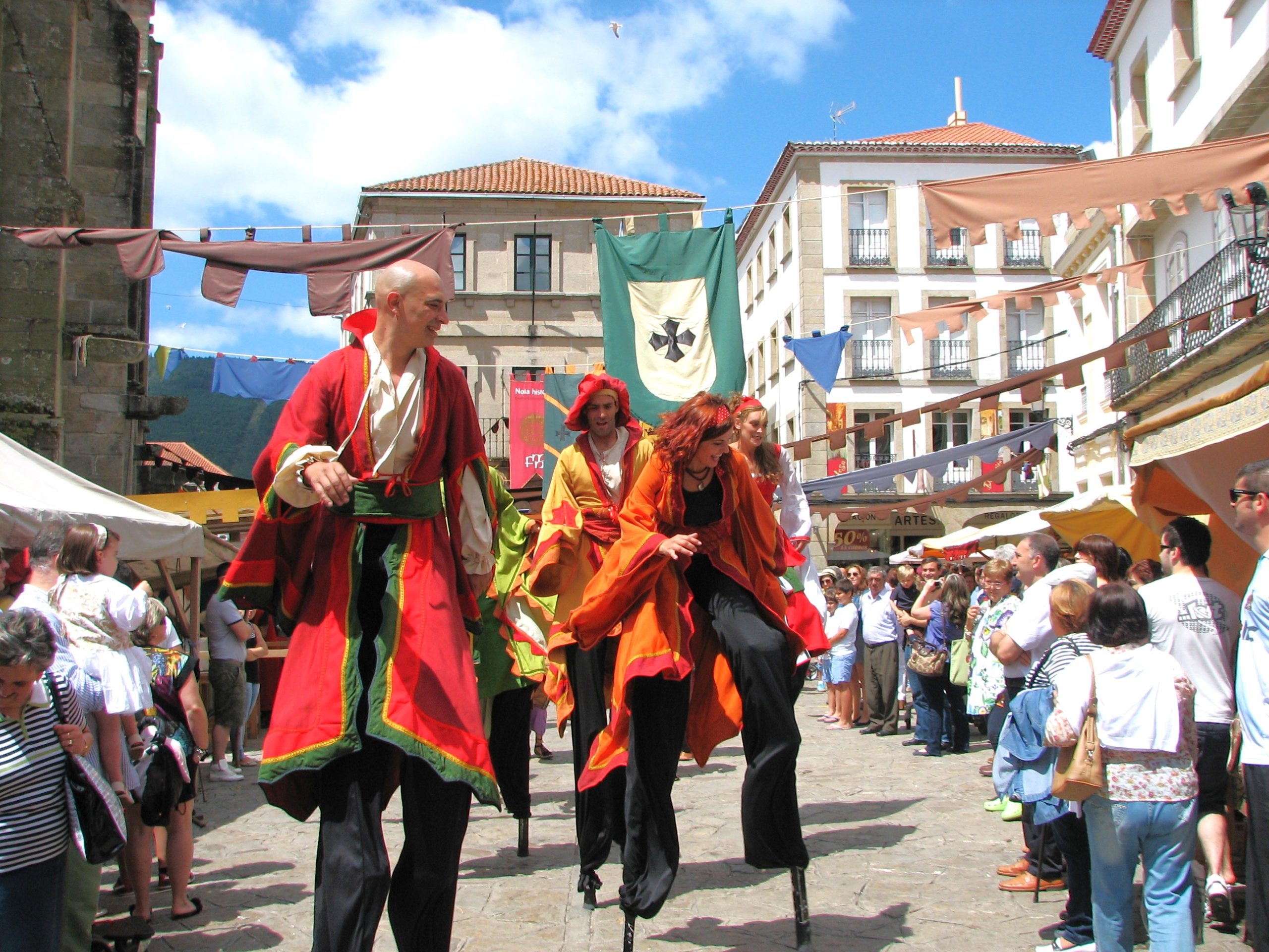 Varios zancudos con túnicas rojas y naranjas desfilan por una plaza soleada.