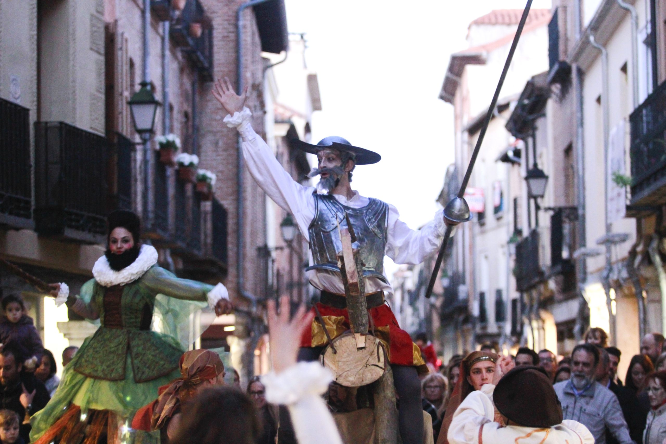 Un actor que interpreta a Don Quijote, con armadura metálica y lanza, desfila sobre un caballo de madera.
