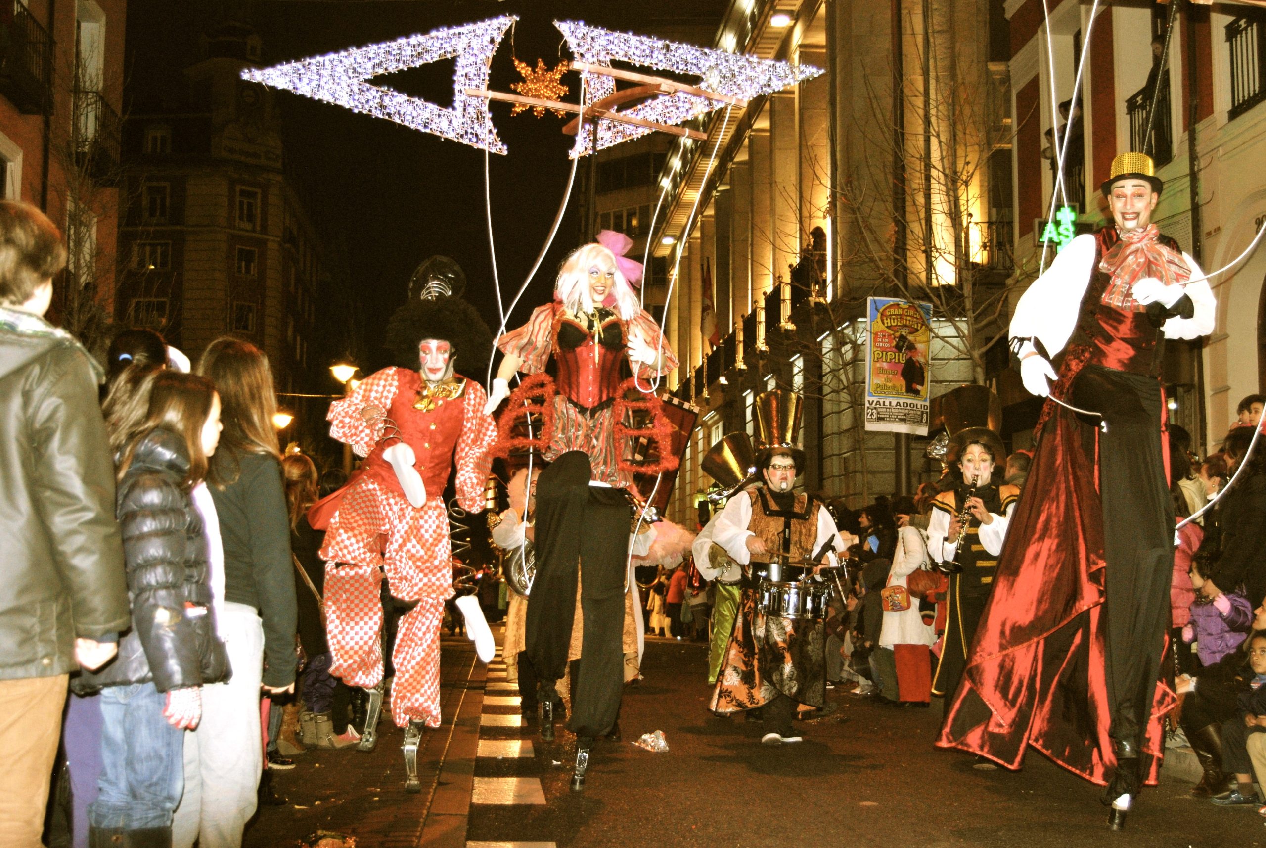 Zancudos disfrazados de marionetas gigantes desfilan por una calle iluminada.