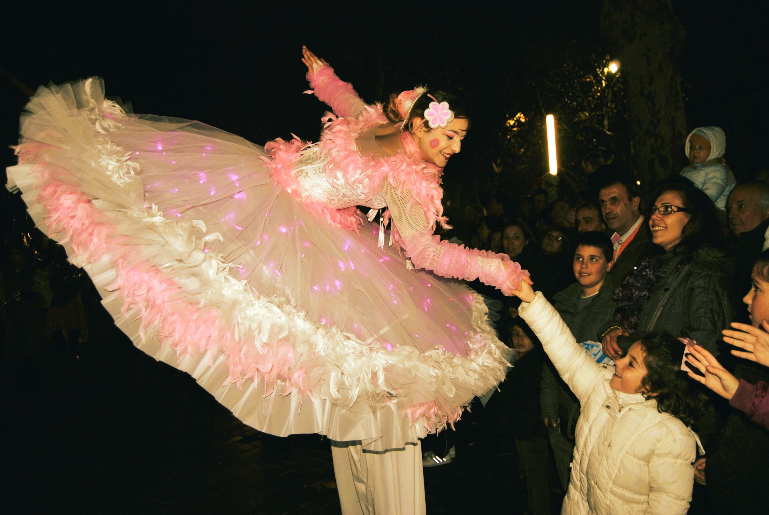 Una bailarina sobre zancos con un amplio vestido rosa iluminado por luces LED