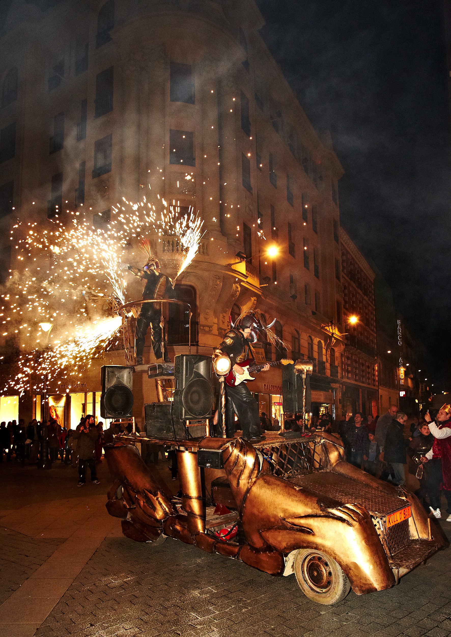 Un vehículo artístico de tono cobrizo y formas aerodinámicas avanza por una calle bajo la noche.